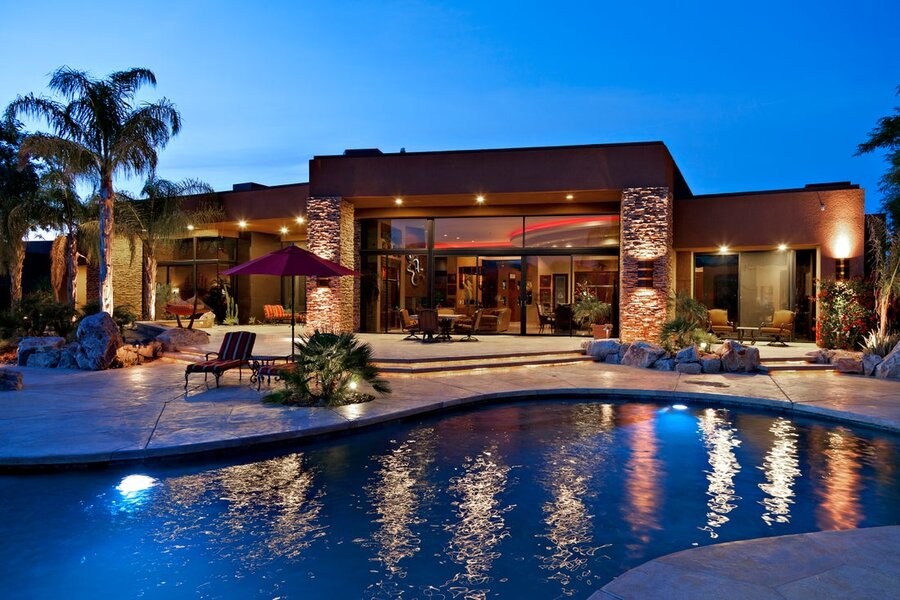 A home’s exterior and pool illuminated by landscape lighting.