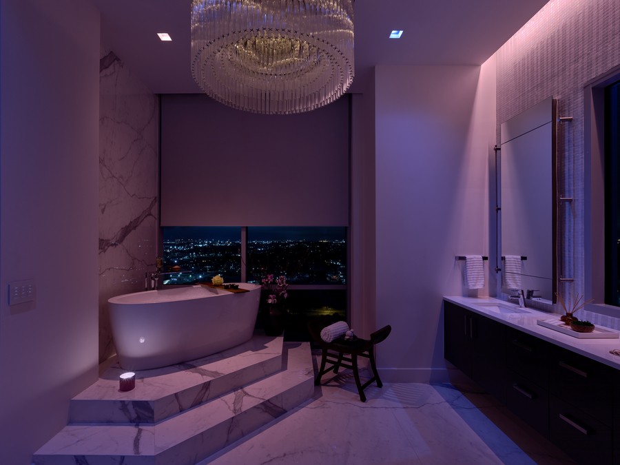 A bathroom illuminated in violet with a Lutron shade partially drawn by a soaking tub. 