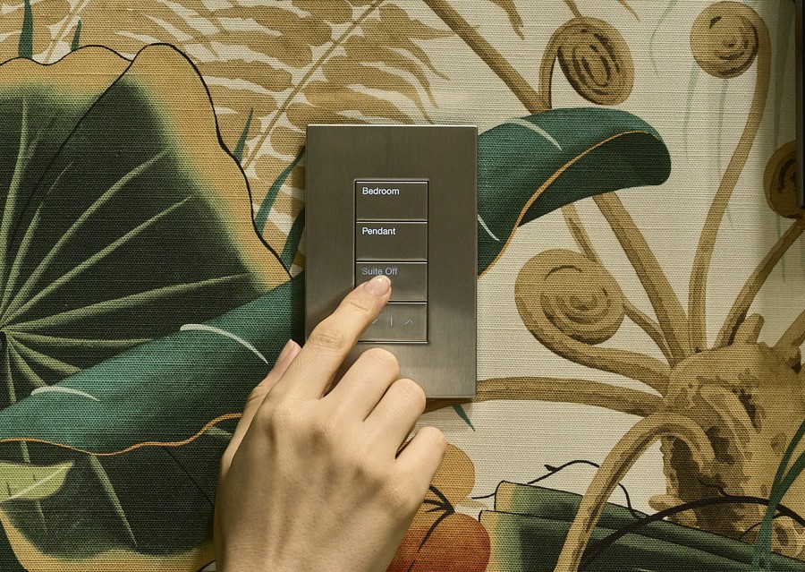 Hand tapping a Lutron lighting keypad on a wallpapered wall. 