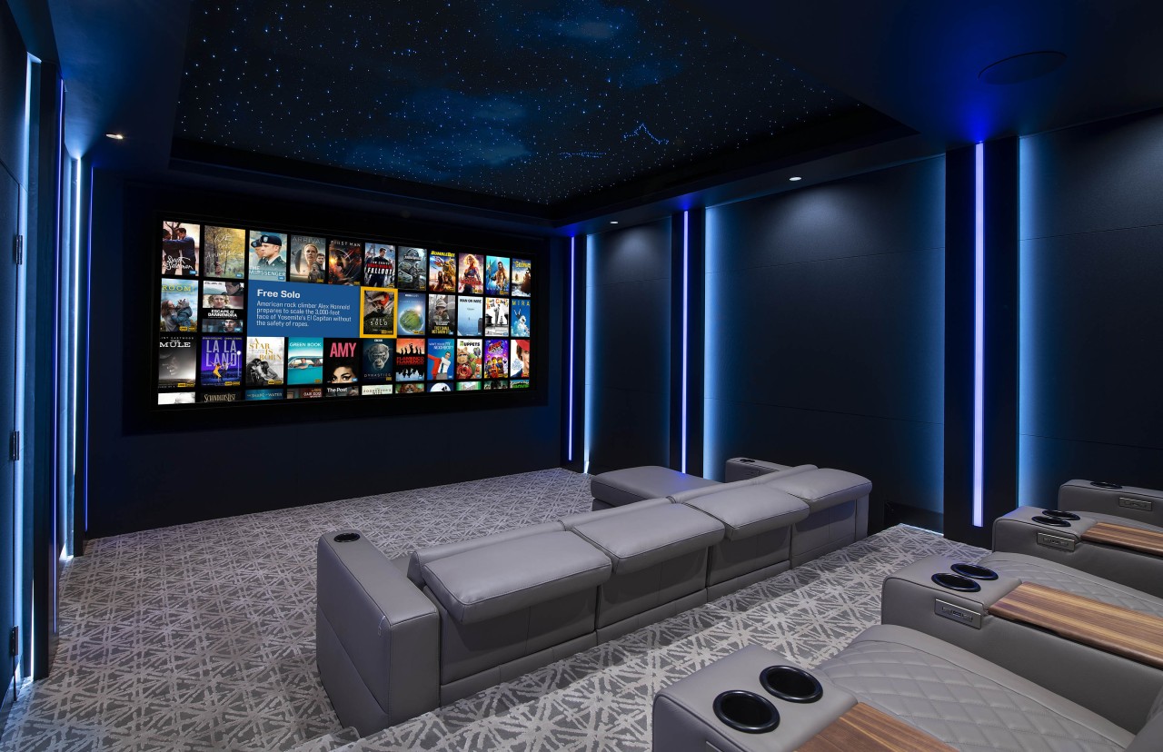 A modern, luxury home theater with linear lighting and a Kaleidescape menu on screen.